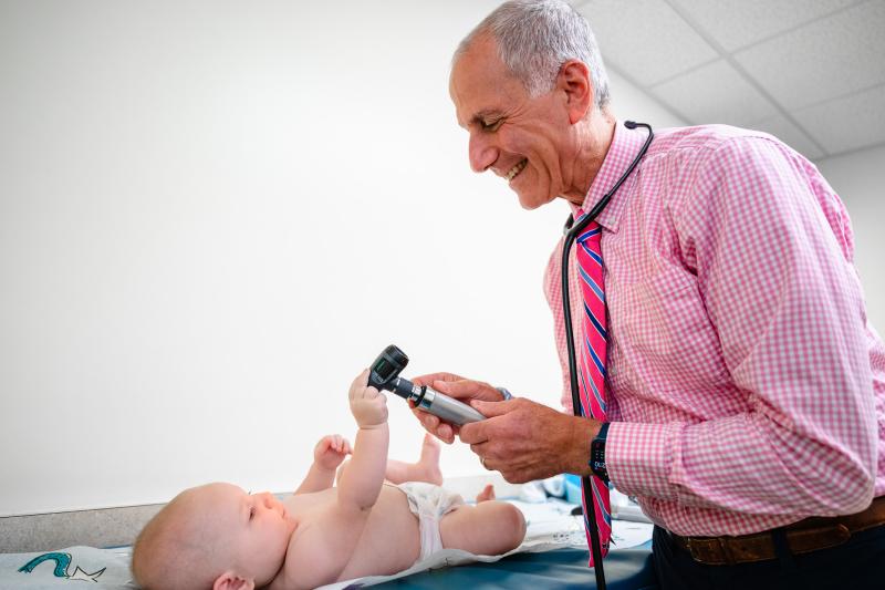 an older doctor looking down at a newborn on a table with a light